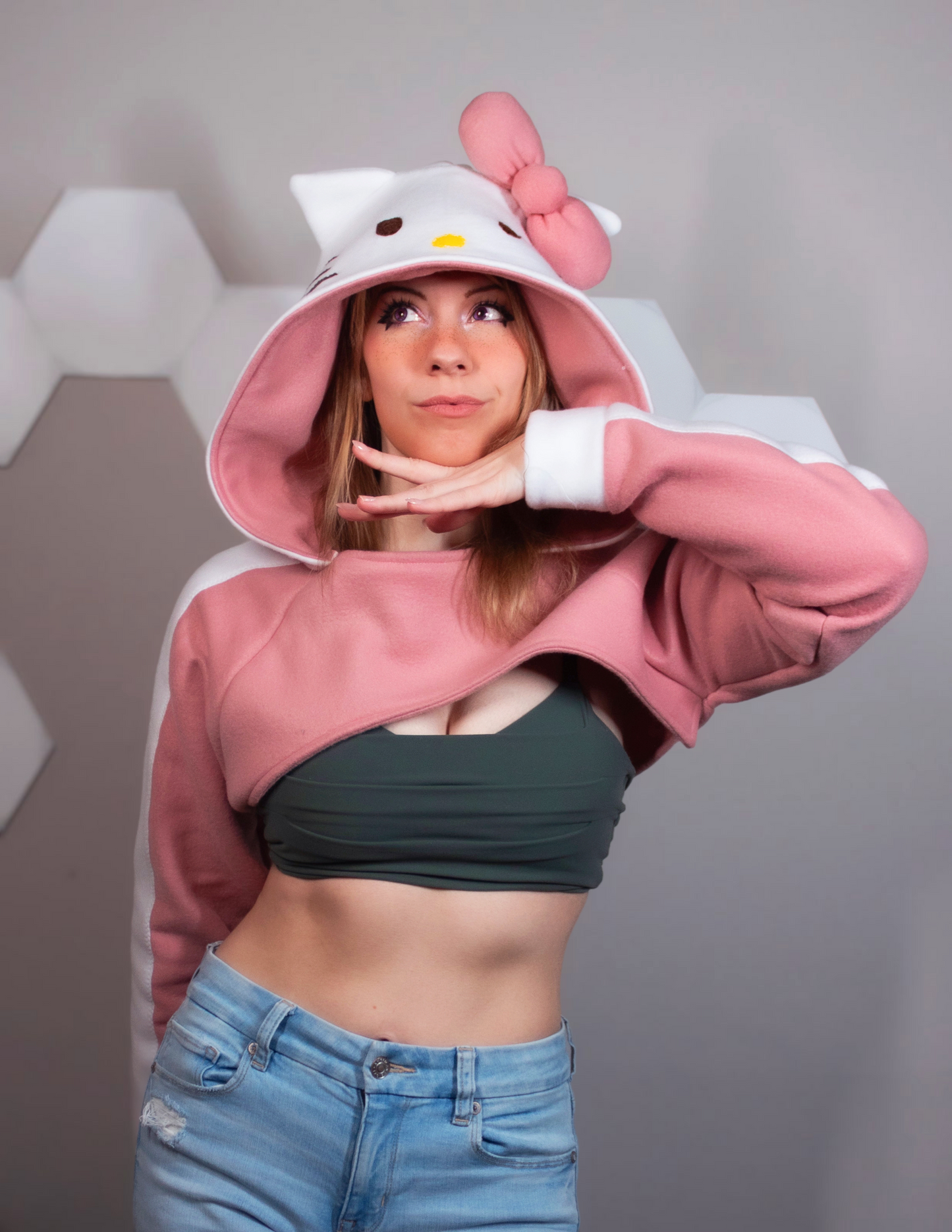 Girl wearing a handmade cosplay shrug inspired by Hello Kitty. It is pink and white with Hello Kitty's face and bow on the hood. Very kawaii cute.