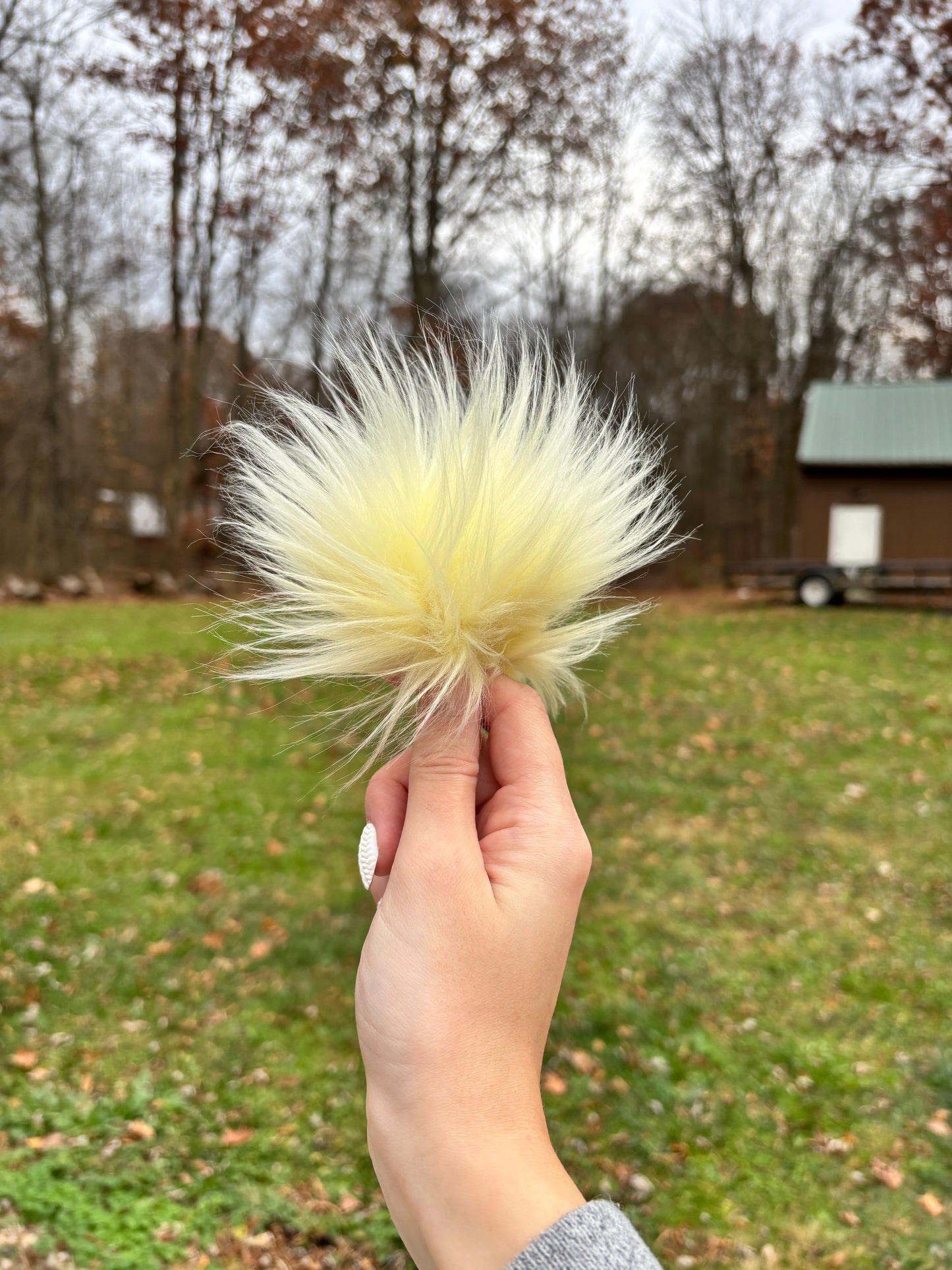 Hand Holding a faux fur pom in light yellow.