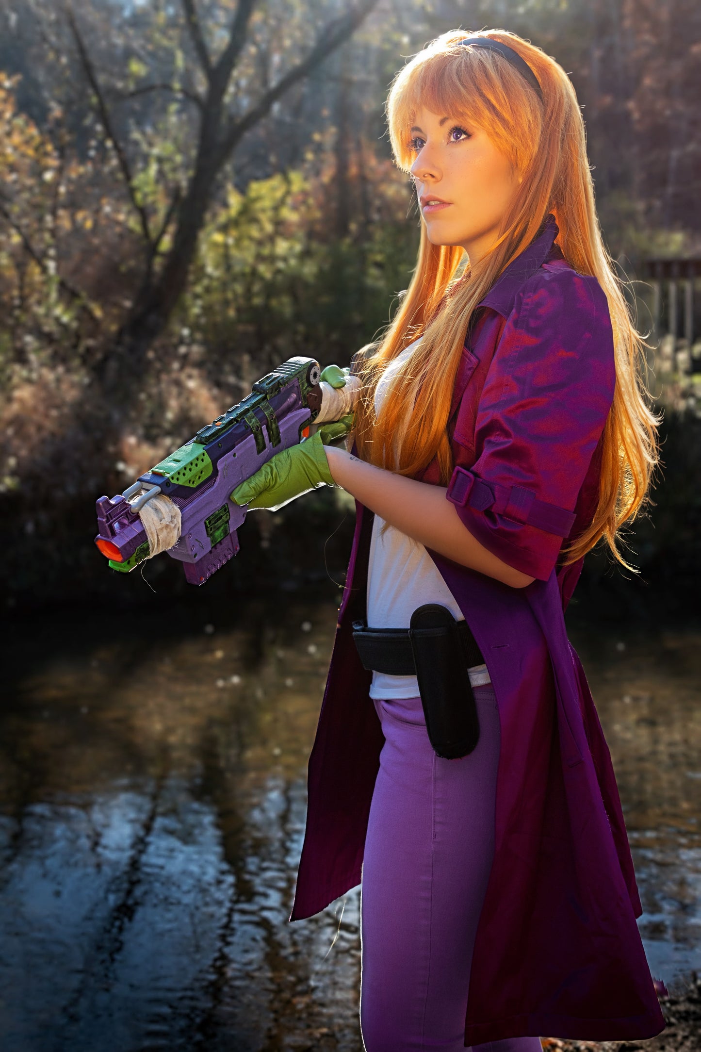 Person in a purple outfit holding a colorful toy gun outdoors near water. Inspired by Daphne from Scooby Doo and the Apocolyptic Comic Book Series.
