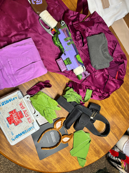 Assorted items including a purple jacket, green gloves, and a first aid kit on a wooden table. Inspired by Daphne from Scooby Doo and the Apocolyptic Comic Book Series.