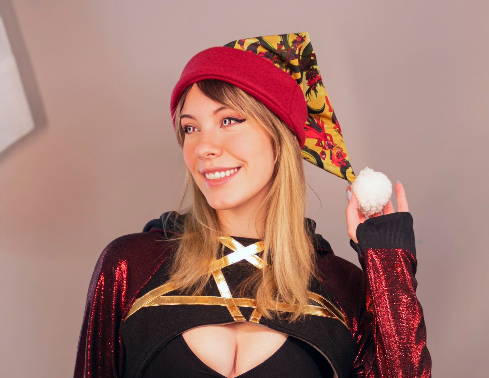 Woman wearing a colorful outfit with a red hat and holding a white ball against a neutral background. Print is of Alastor from Hazbin hotel.