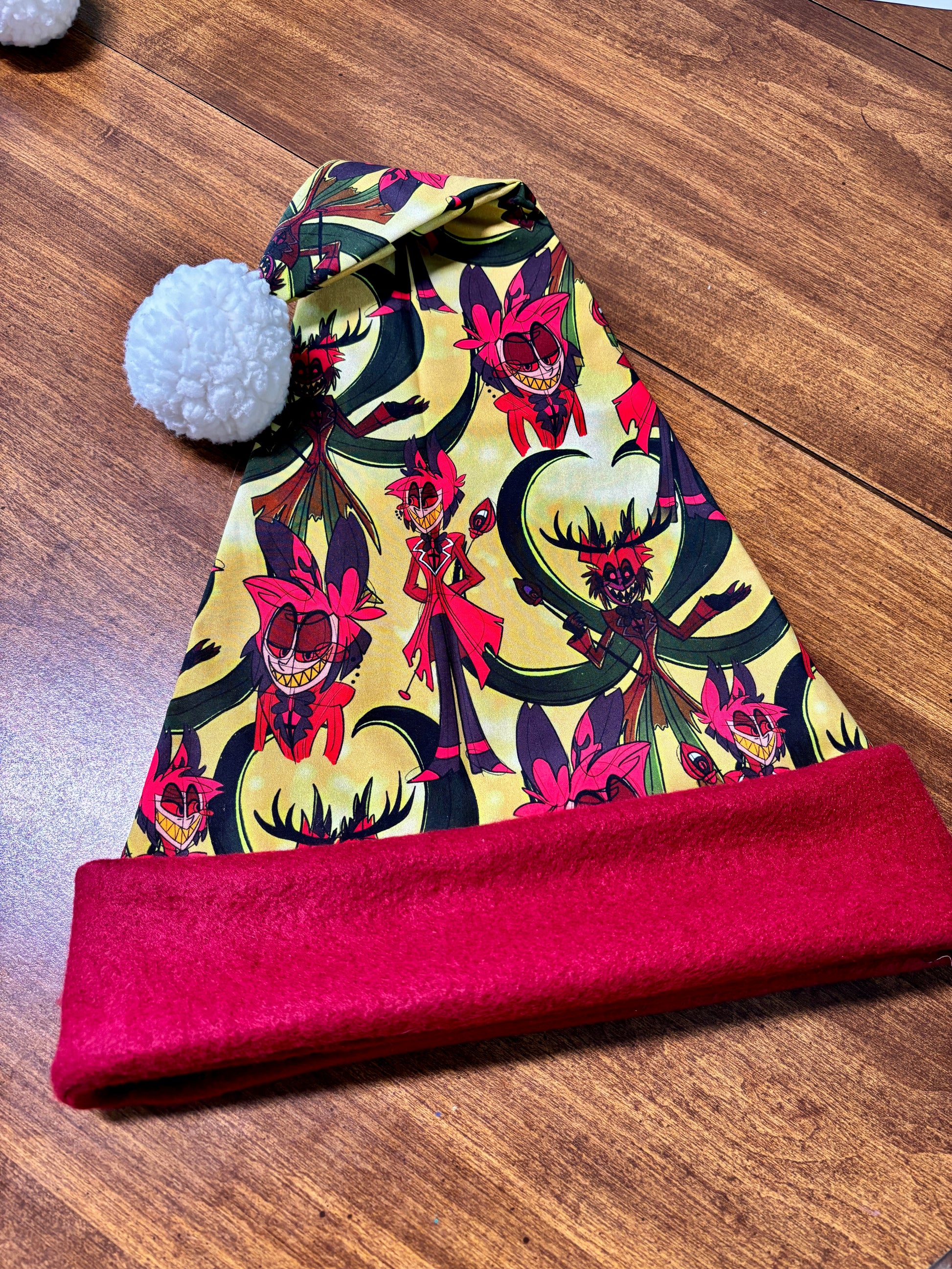 Colorful patterned beanie with a red band on a wooden surface. Print is of Alastor from Hazbin hotel.