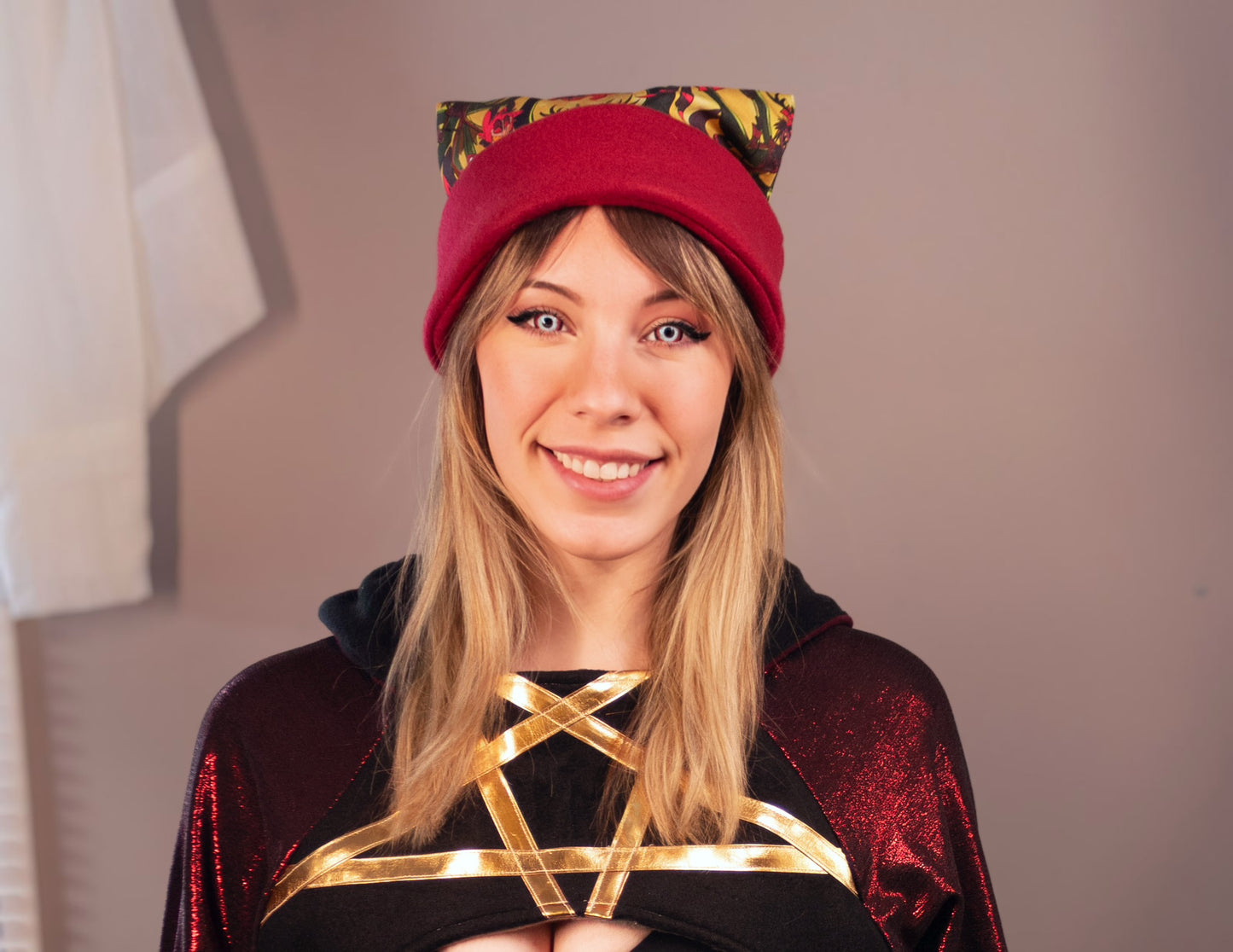 Person wearing a red hat with cat ears and a black outfit with gold accents. Print is of Alastor from Hazbin hotel.