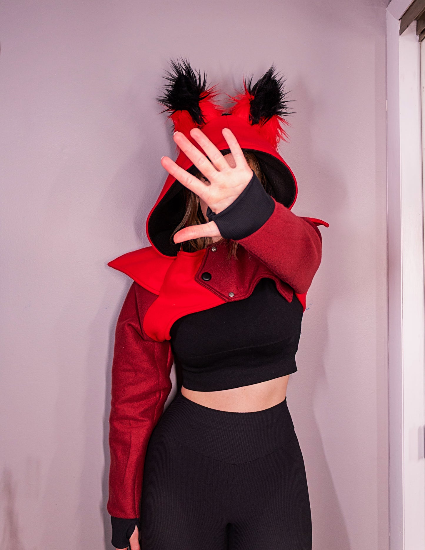 Person wearing a red and black outfit with a hood and fur details against a plain background. Inpired by Aastor from Hazbin Hotel.