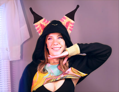 Person wearing a black hoodie with colorful accents and decorative Hood against a light purple background. Inspired by Queen Bee from Helluva Boss. 