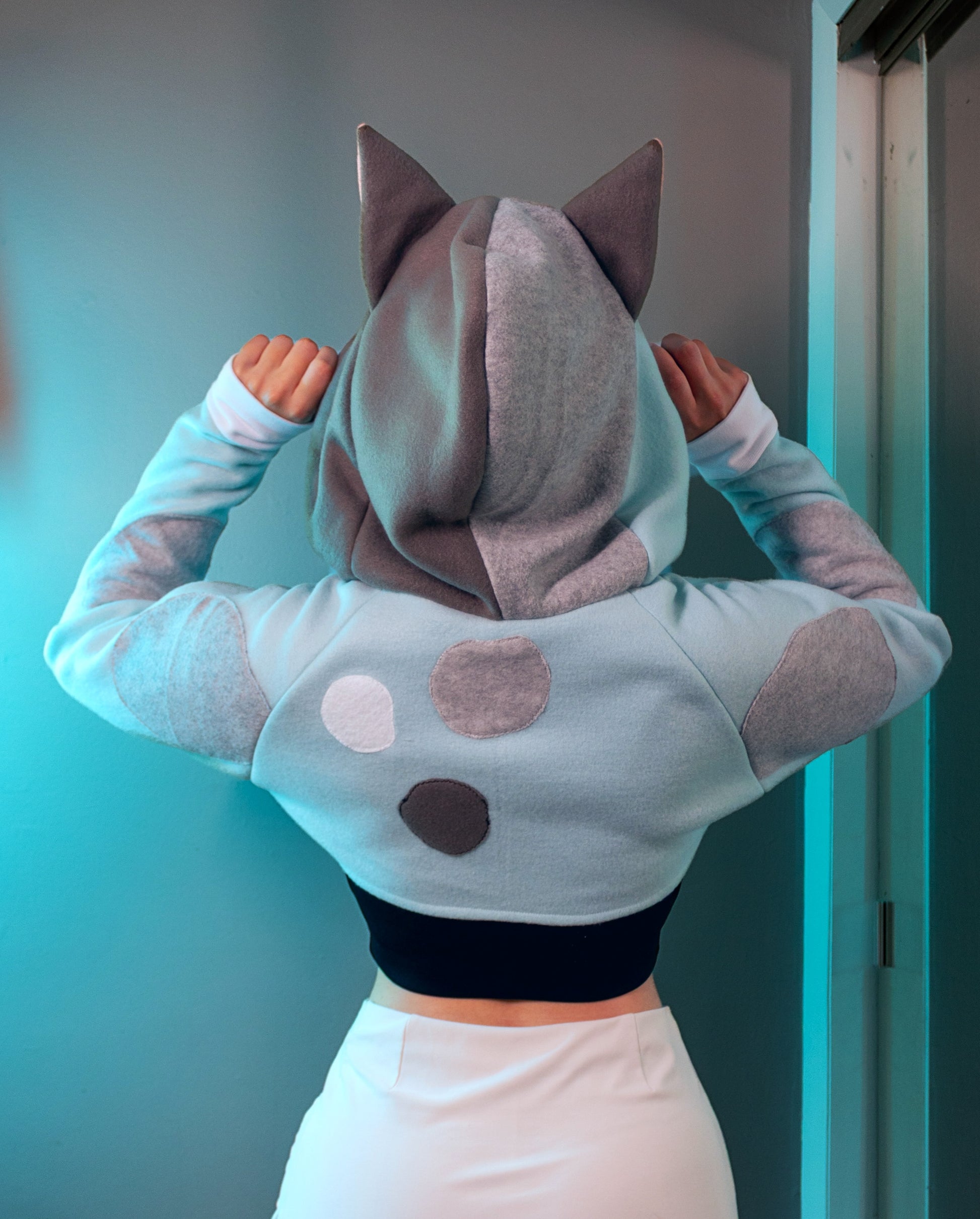 Person wearing a cosplay shrug inspired by Muffin from Bluey. It is light blue with multi-colored spots. 