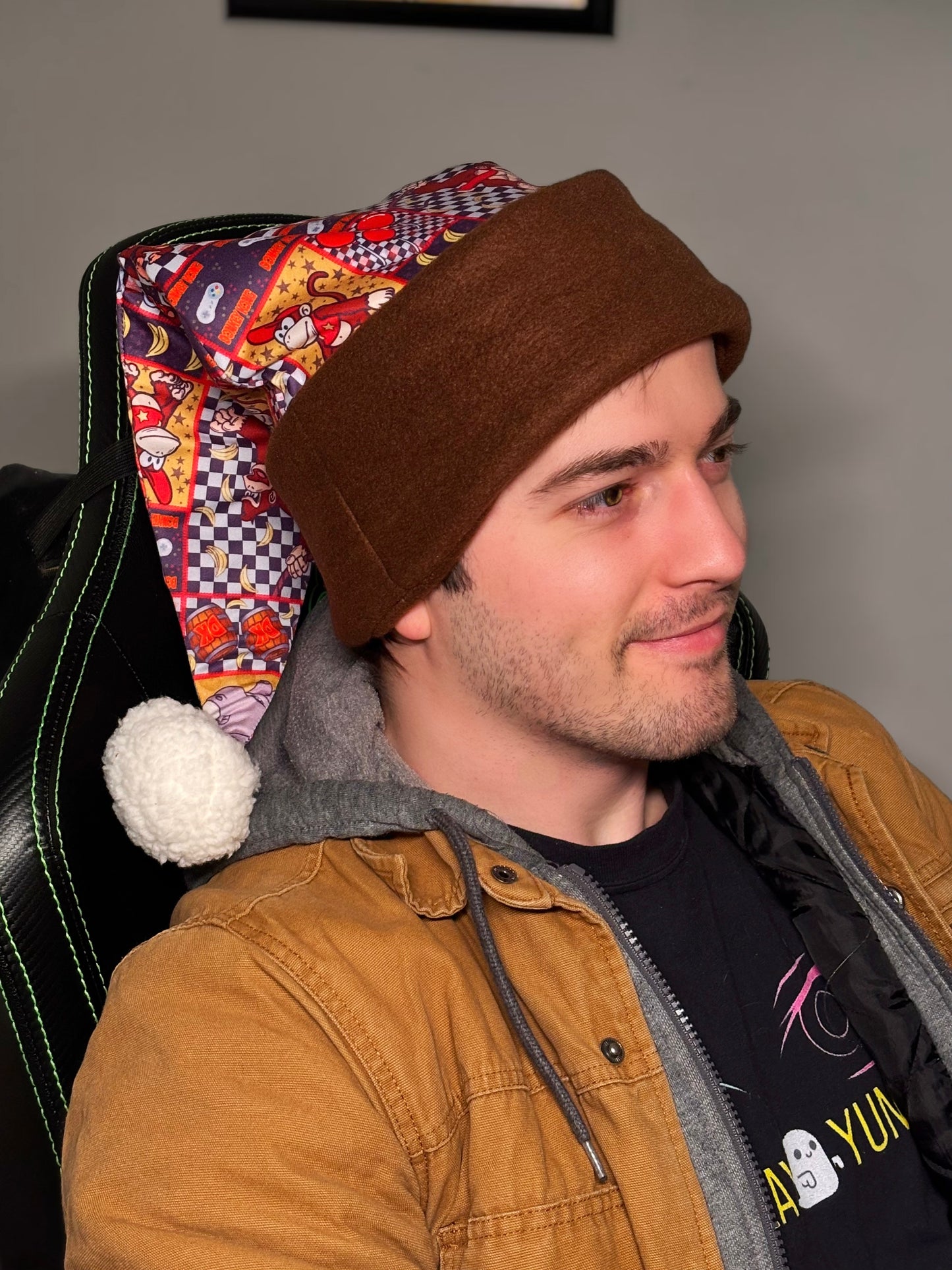 Man wearing a brown beanie and tan jacket sitting on a chair with colorful backrest. Inspired by Donkey Kong