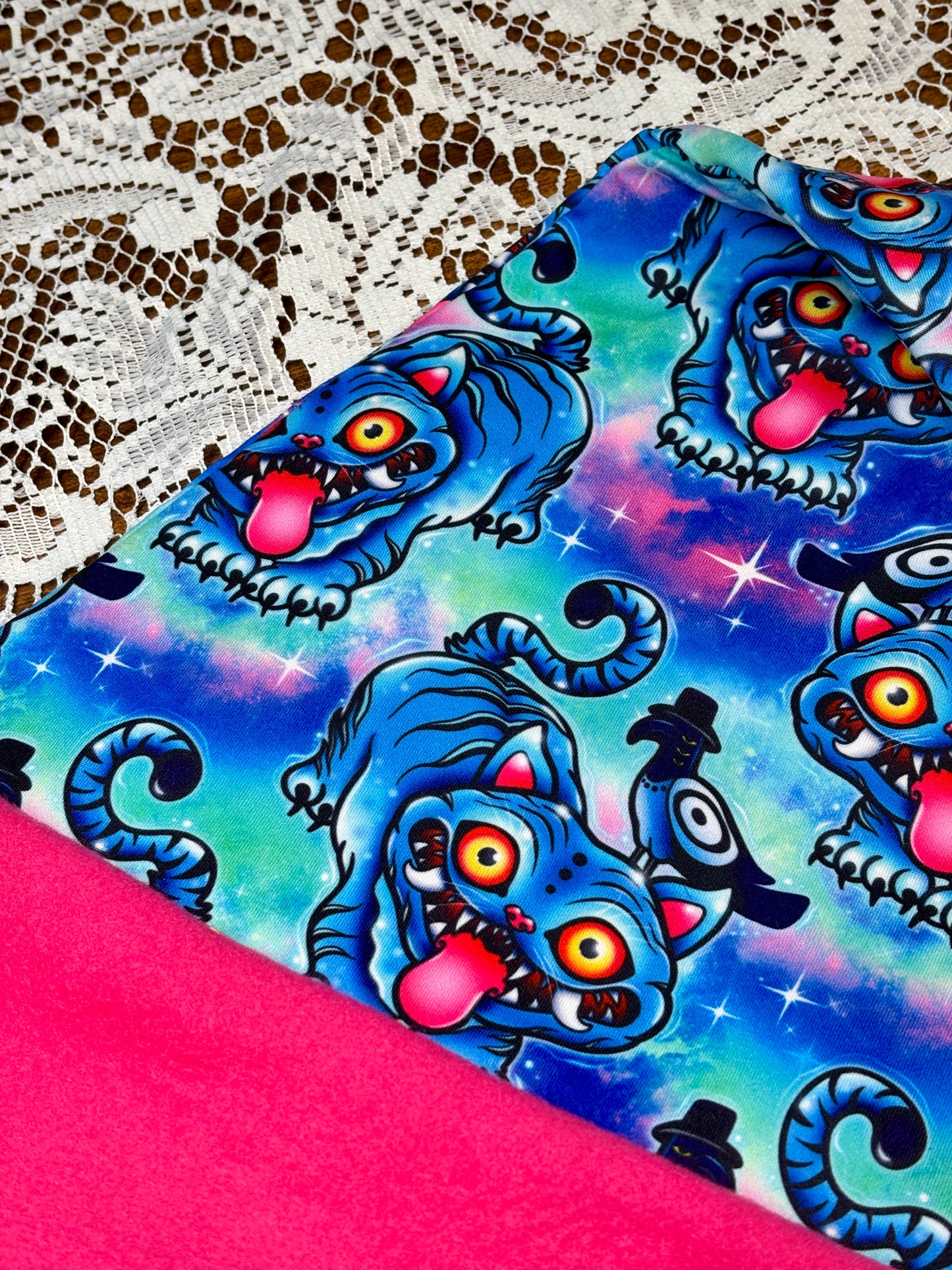 Pink fabric with a blue patterned fabric on top, on a lace background. Pattern is of Deroy Tiger from Kpop Demon Hunters