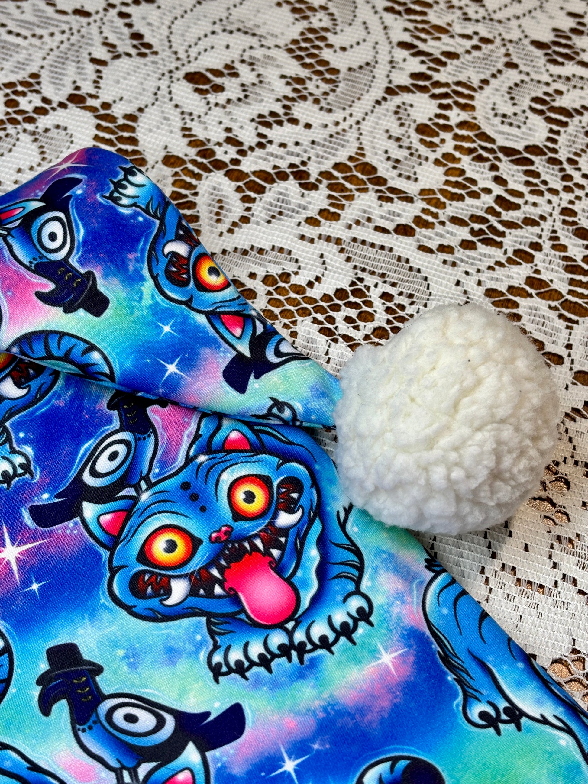 Pink fabric with a blue patterned fabric on top, on a lace background. Pattern is of Deroy Tiger from Kpop Demon Hunters. Close up of Sherpa Pom