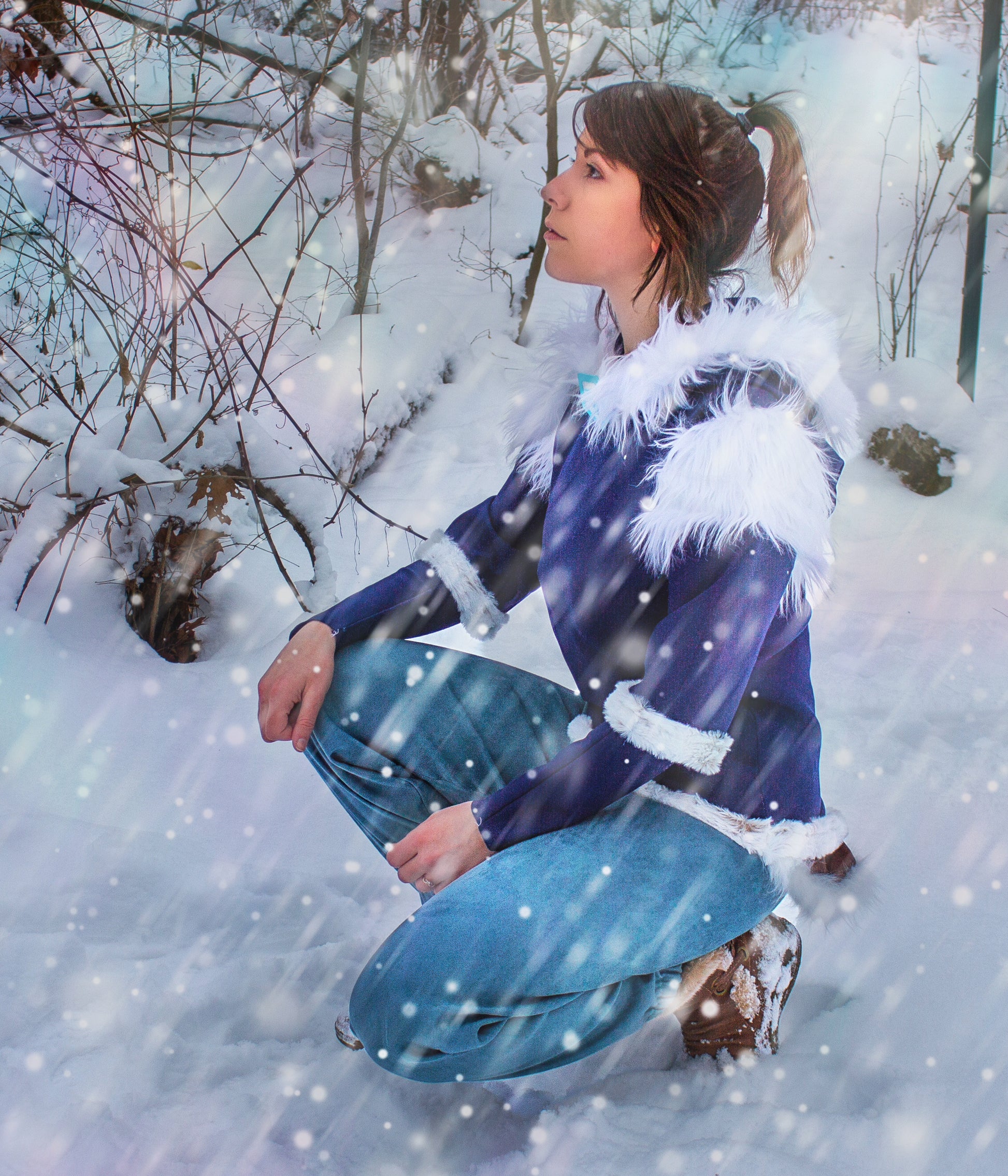 Person in a blue coat with white fur trim sitting in a snowy forest
