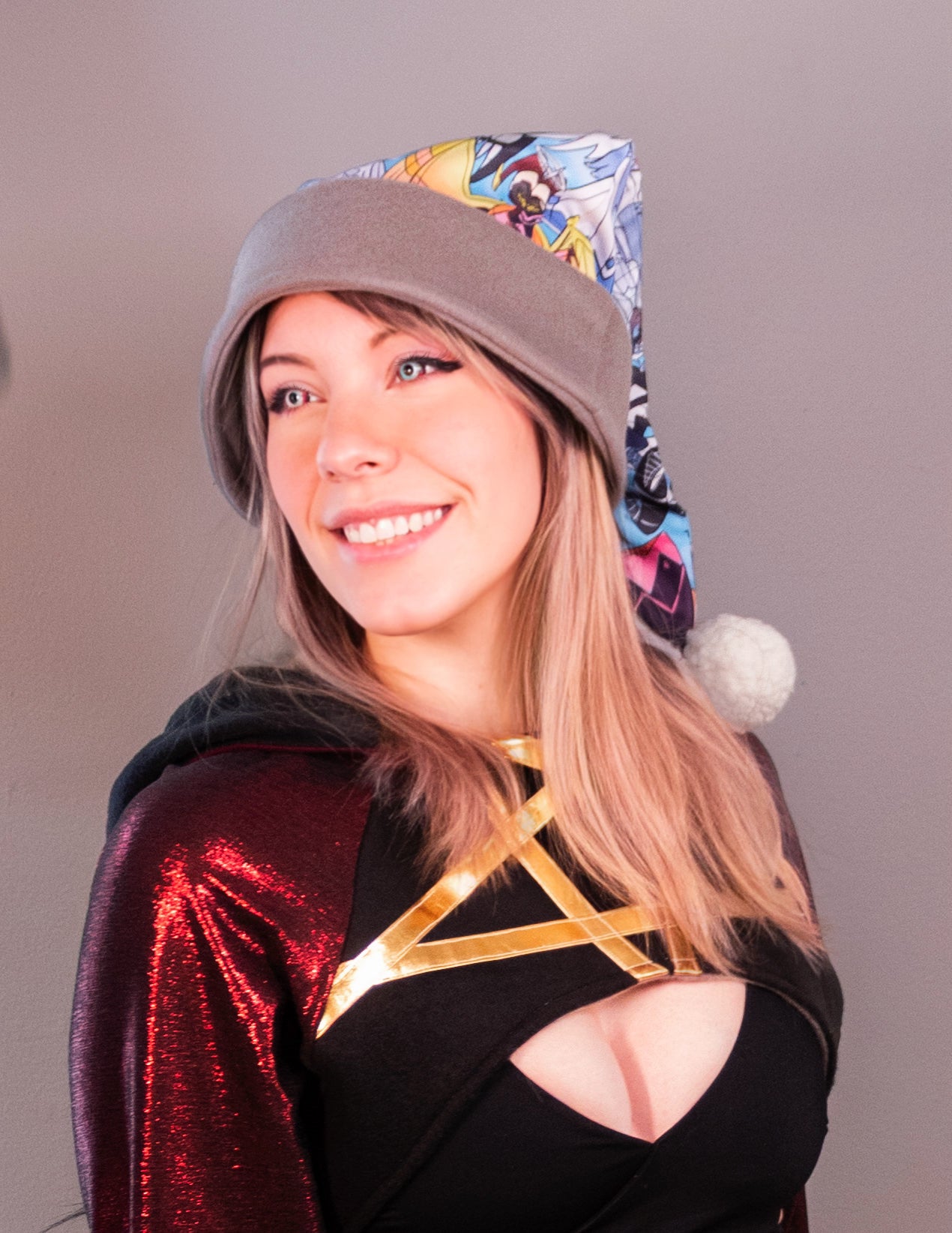 Person wearing a colorful hooded garment with a plain background. Print  of the Santa hat has Hazbin Hotel characters on it like Adam and Lute.