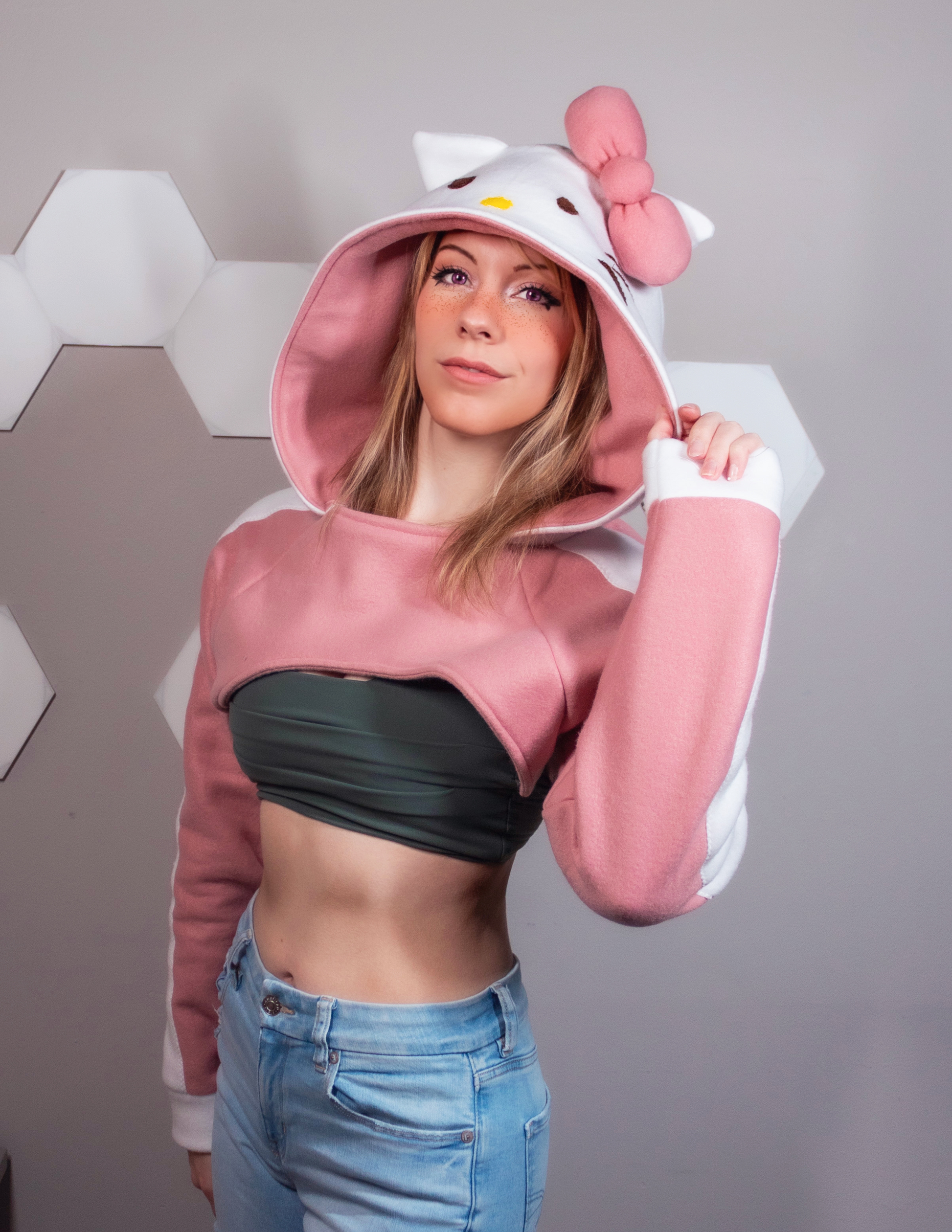 Girl wearing a handmade cosplay shrug inspired by Hello Kitty. It is pink and white with Hello Kitty's face and bow on the hood. Very kawaii cute.