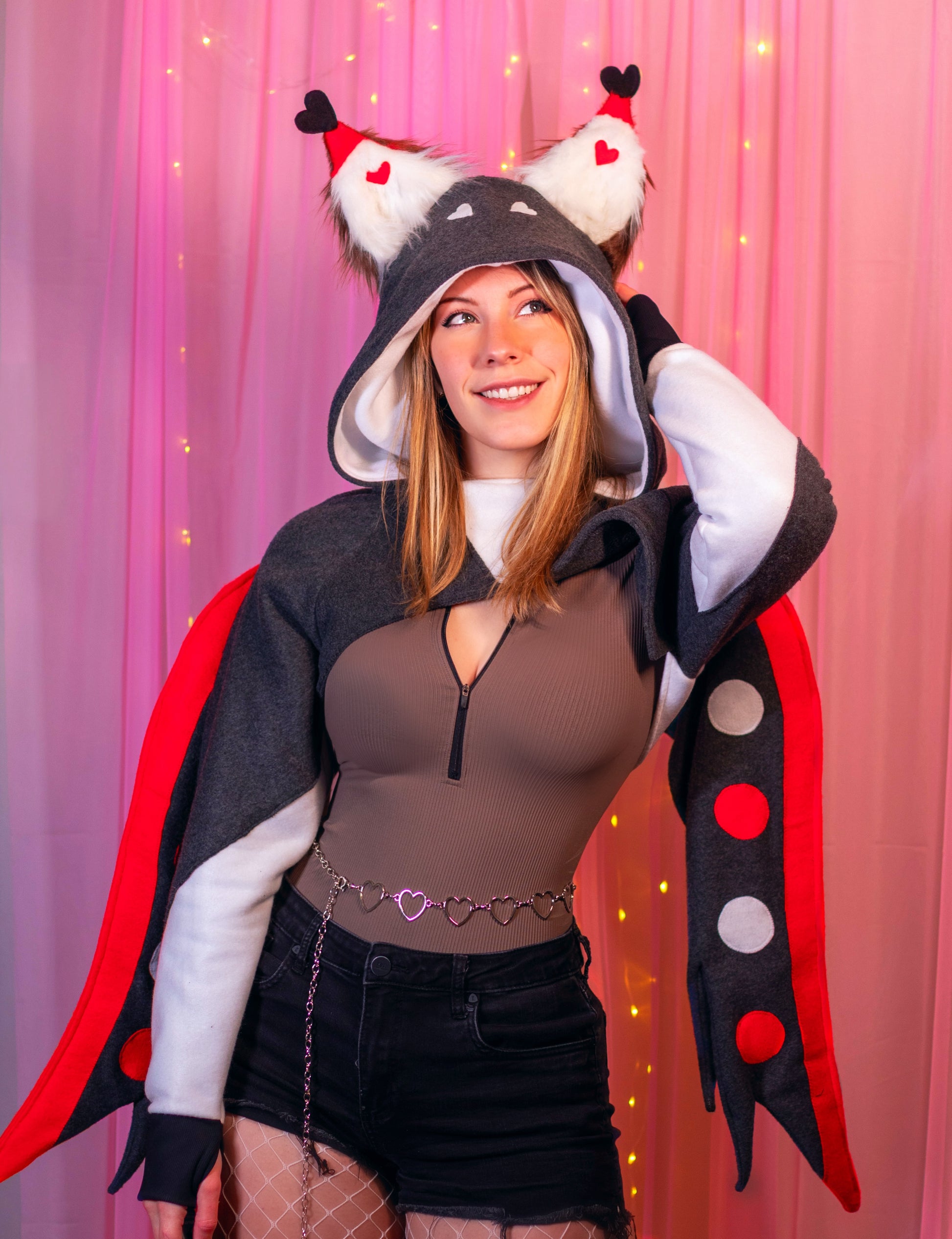 Woman wearing a Husk from Hazbin Hotel inspired shrug against a pink background. Another up close shot showing the cropped hoodie and wings.
