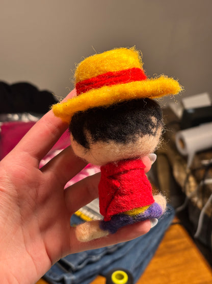 Colorful felted finger puppet held in a hand with a blurred background. Inspired by Luffy from One Piece. 