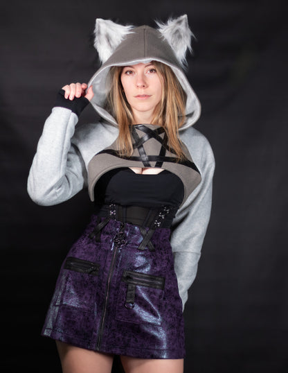 Person wearing a gray hoodie with wolf ears and a purple skirt on a black background. Cropped hoodie is inspired by Loona from Helluva Boss