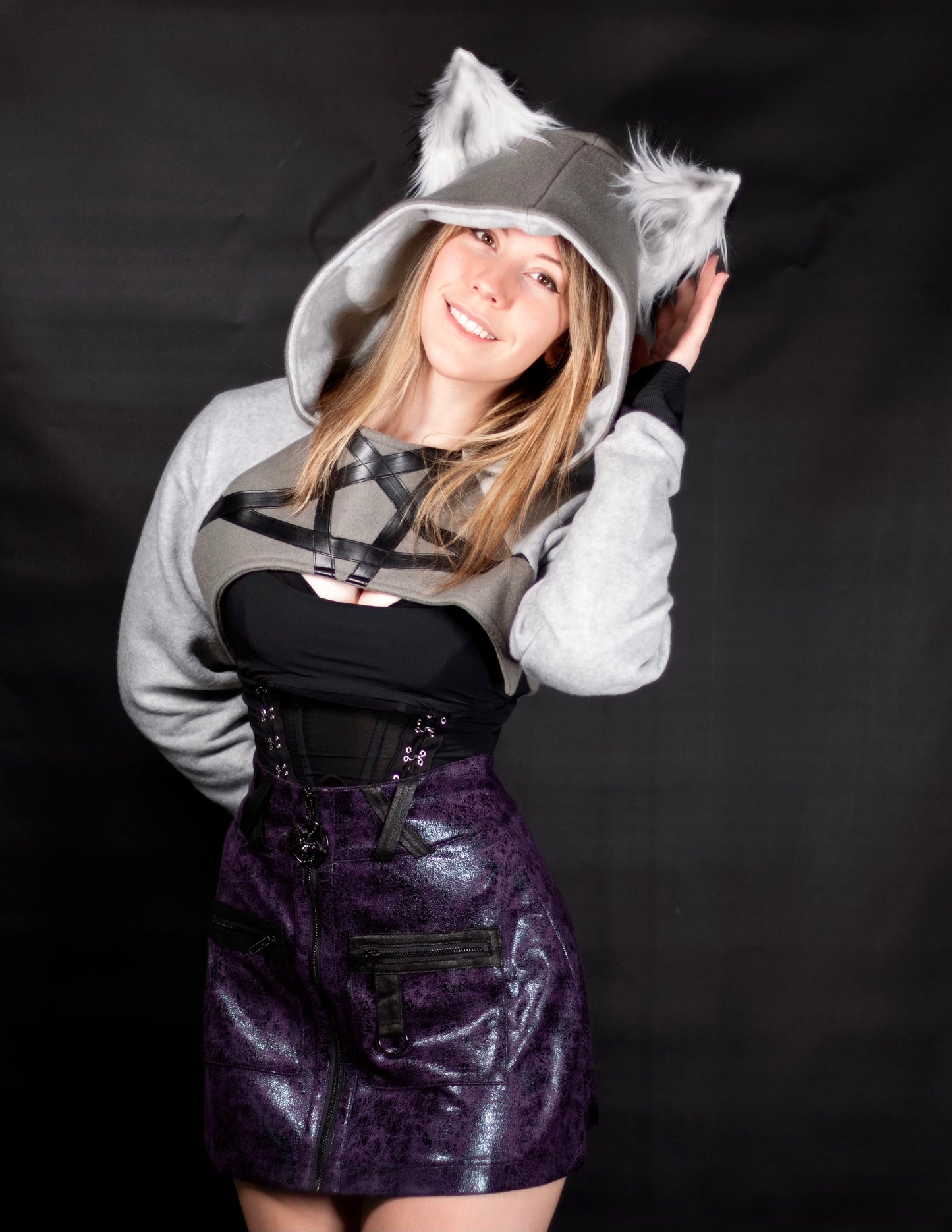 Person wearing a gray hoodie with wolf ears, black top, and purple skirt on a black background. Cropped Hoodie is inspired by Loona from Helluva Boss