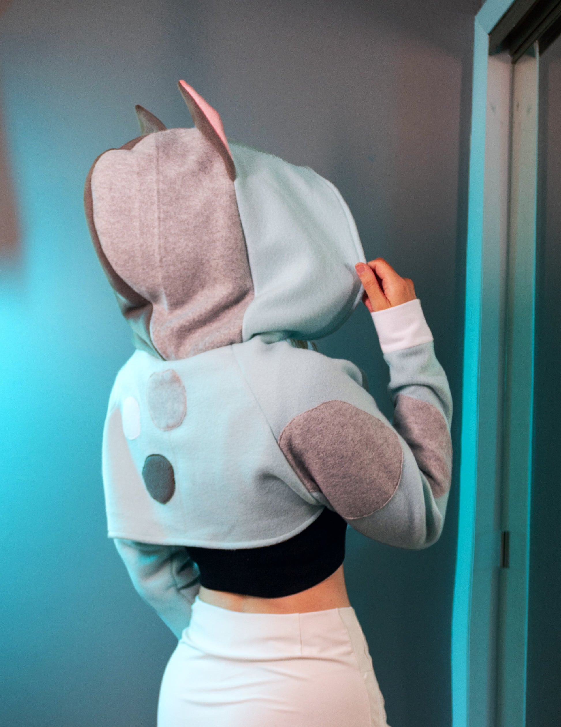 Person wearing a cosplay shrug inspired by Muffin from Bluey. It is light blue with multi-colored spots. 