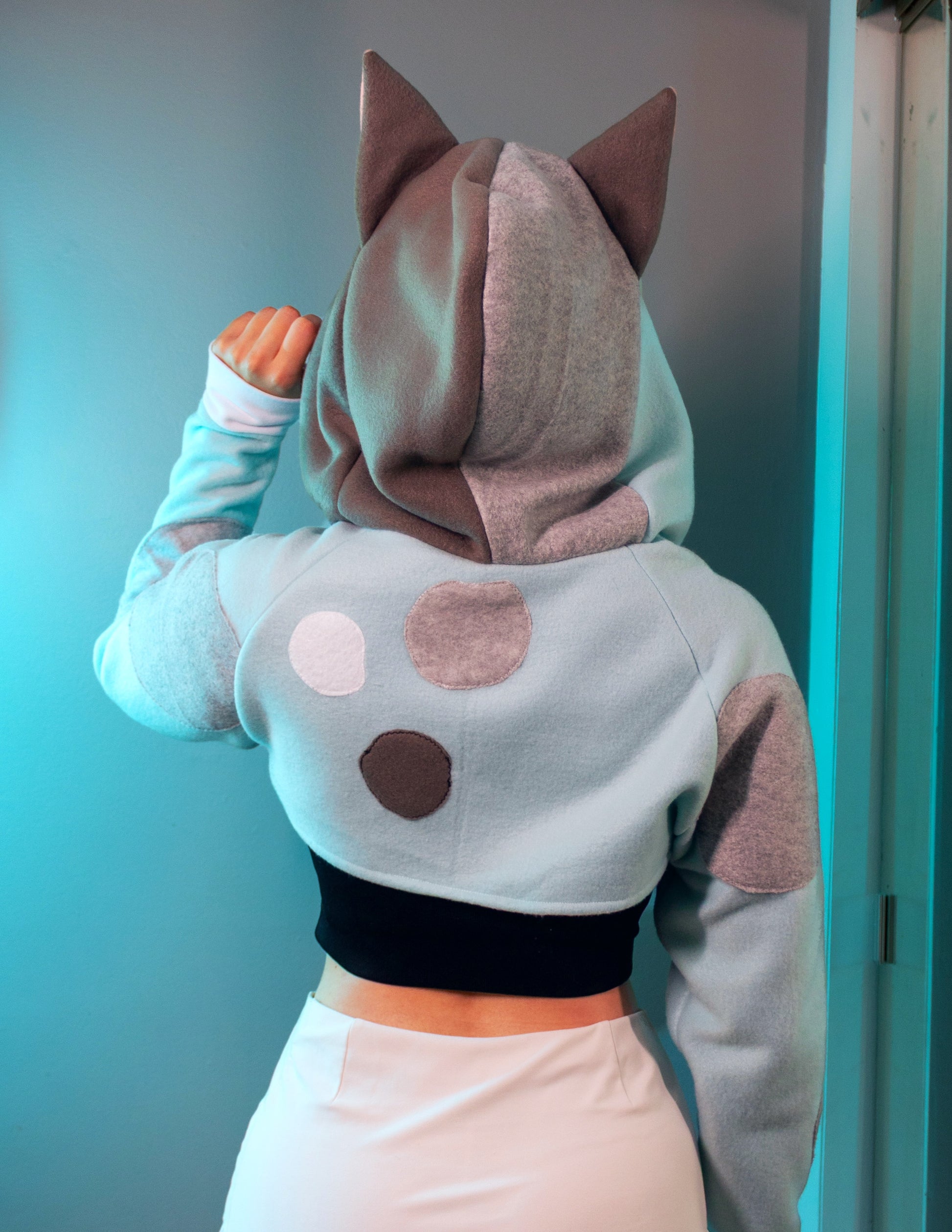 Person wearing a cosplay shrug inspired by Muffin from Bluey. It is light blue with multi-colored spots. 