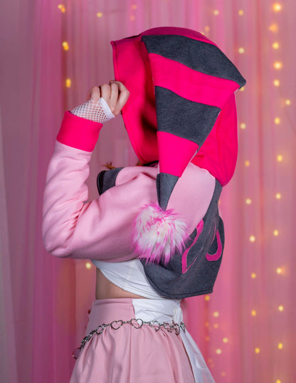 Woman wearing a Valentine's Day shrug inspired by Fizzarolli from Helluva Boss. There is a pink background with twinkle lights. She is wearing a kawaii matching outfit. Focusing on the side of the outfit.