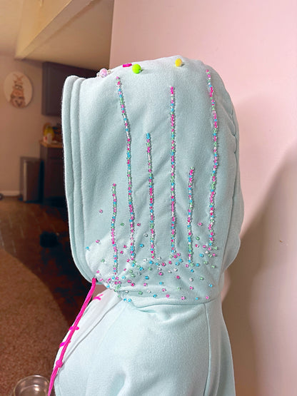 Light blue hoodie with black cuffs and pink drawstrings on a mannequin against a beige background. Inspired by  Vanellope von Schweetz from Disney's Wreck it Ralph. Perfect Cosplay Shrug.