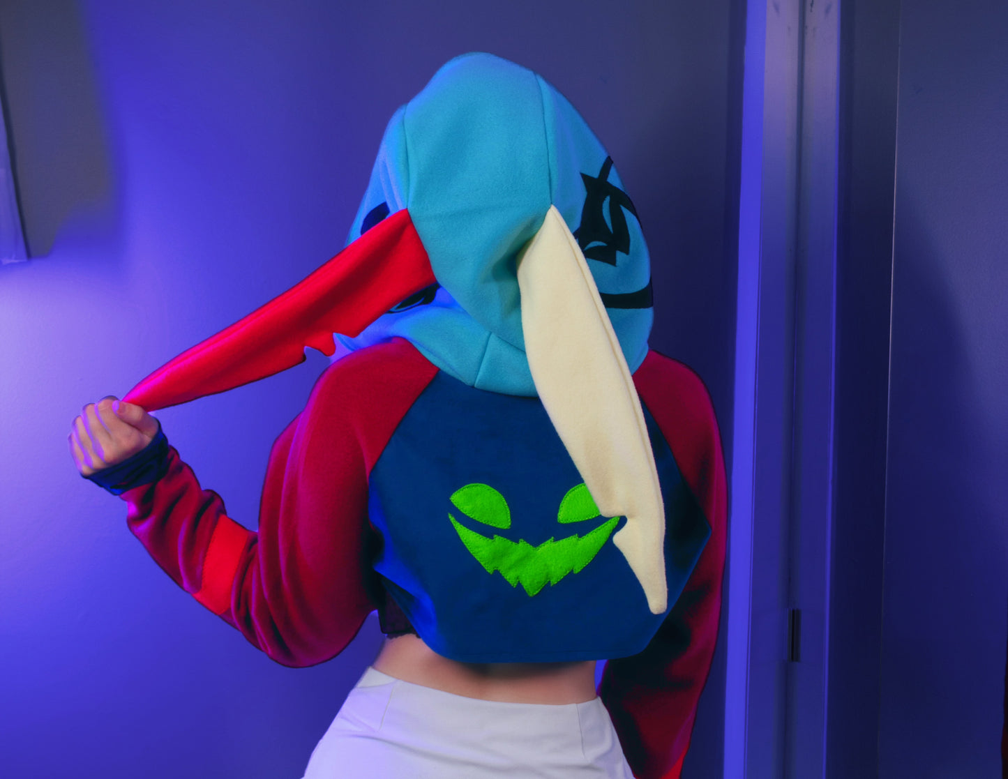 Asmodeus Cosplay cropped hoodie shrug inspired by Helluva Boss shown on a model with a purple background and matching outfit.  Showing ozzie's face on the back