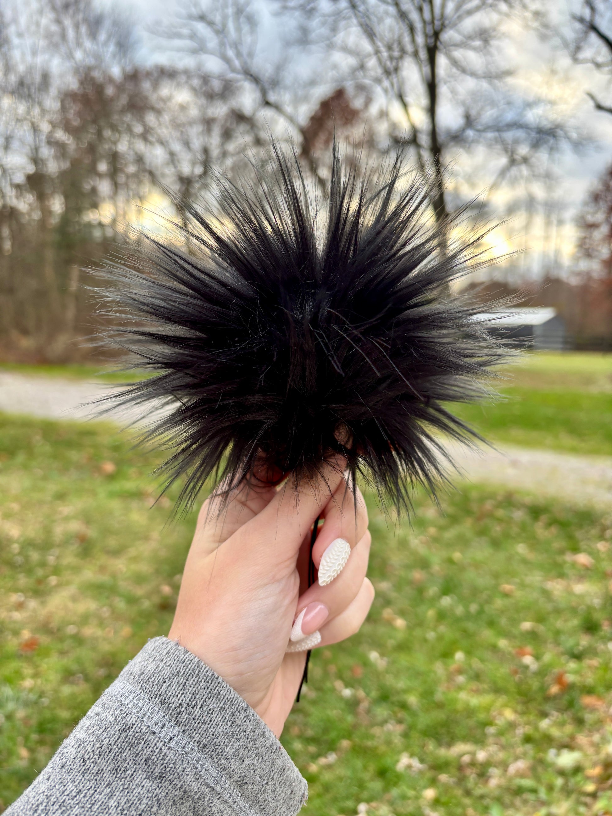 Hand holding a black faux fur pom