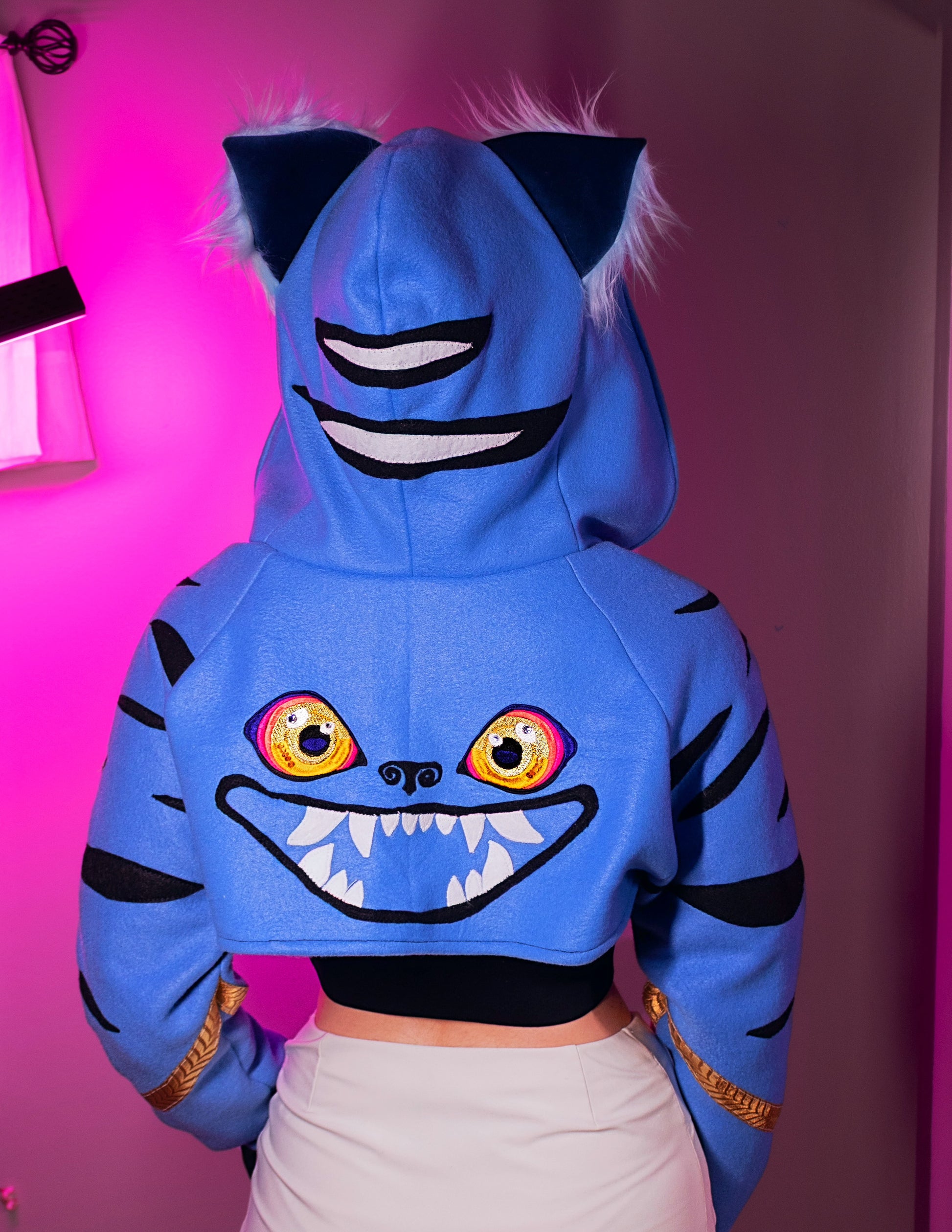 Person wearing a cosplay shrug inspired by Derpy Tiger from Kpop Demon Hunters. It is different shade of blue with  character designs