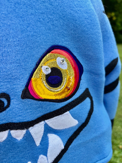 close up of a cosplay shrug inspired by Derpy Tiger from Kpop Demon Hunters. It is different shade of blue with  character designs