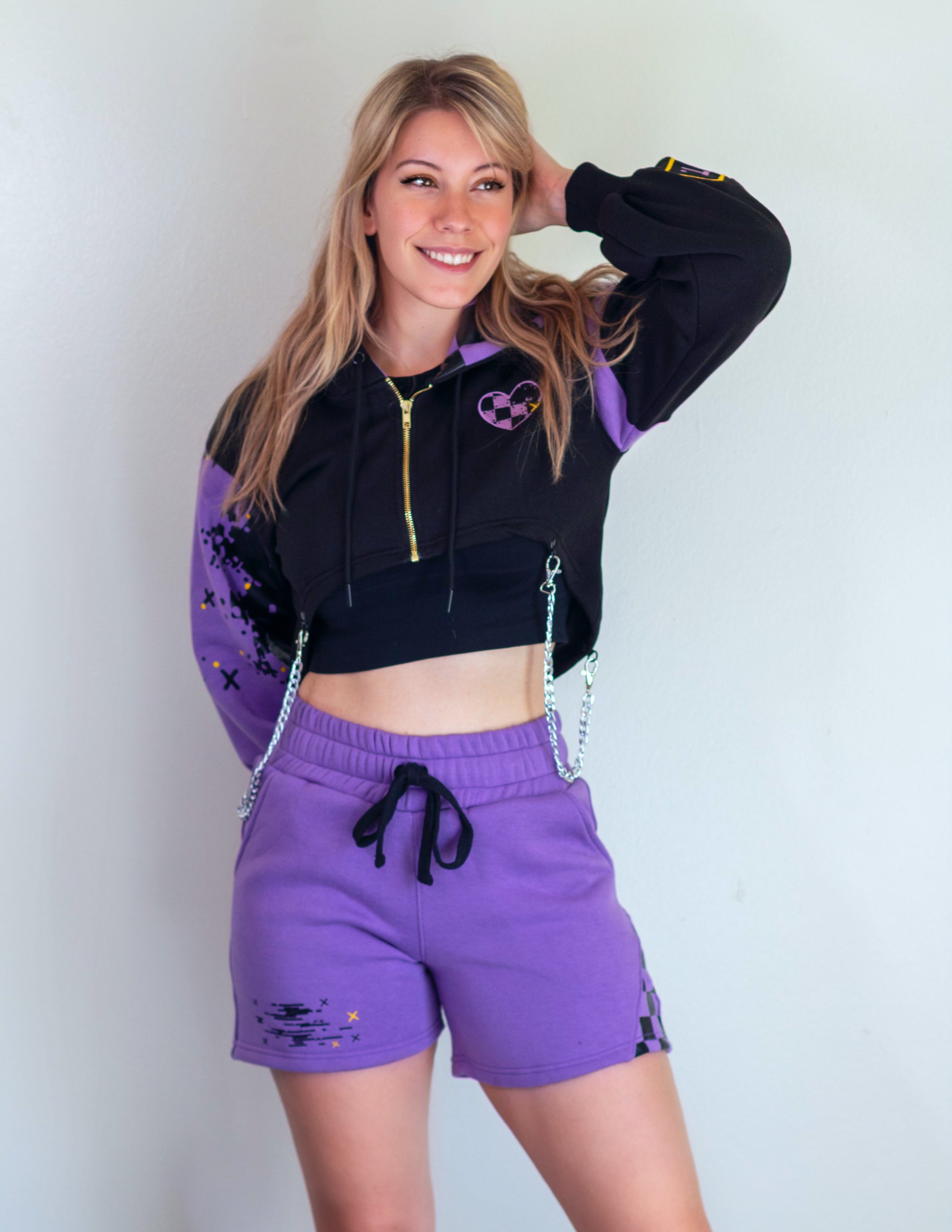 Model is wearing a matching set of shorts and shrug inspired by Jax from the Amazing Digital Circus TADC. The shorts are mainly purple and the top is mainly black with smaller purple details like a checkered heart