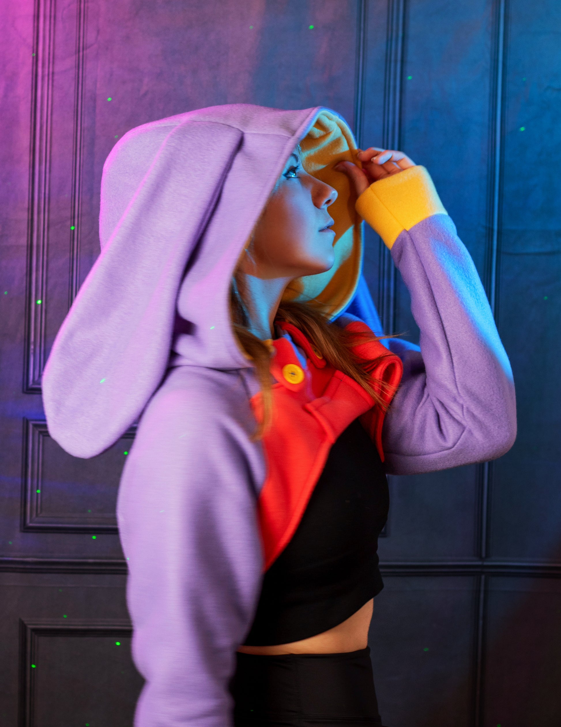 Person wearing a colorful outfit with a hood and bunny ears against a dark background. Inspired by Jax from the Amazing digital circus