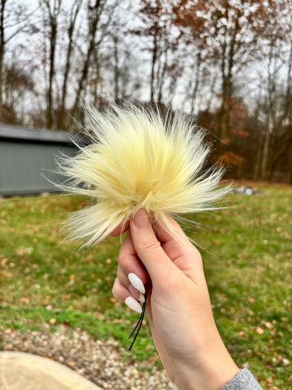 Hand Holding a faux fur pom in light yellow. 