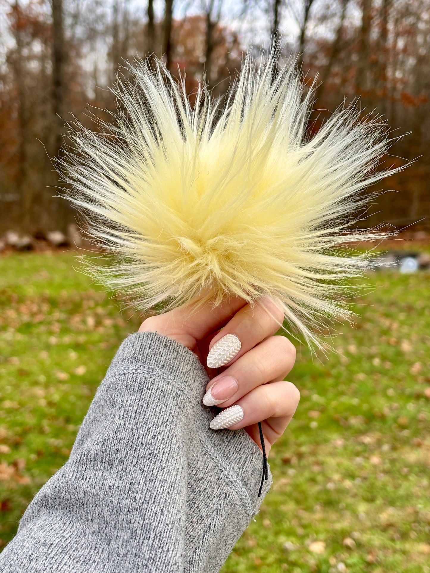 Hand Holding a faux fur pom in light yellow. 