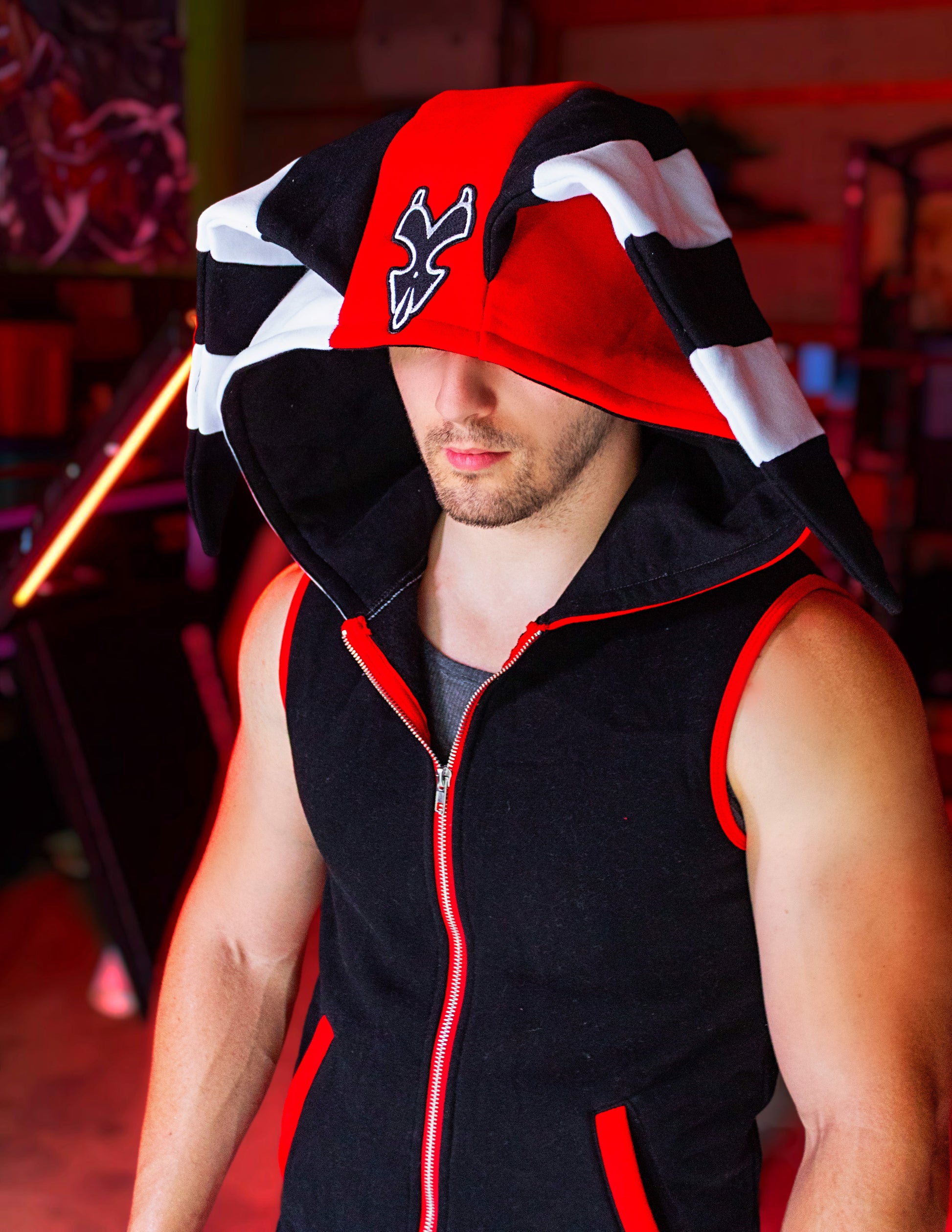 Person wearing a black, red, and white hoodie with a logo on a blurred background. Blitz cosplay inspired by Helluva Boss. sleevelss hoodie