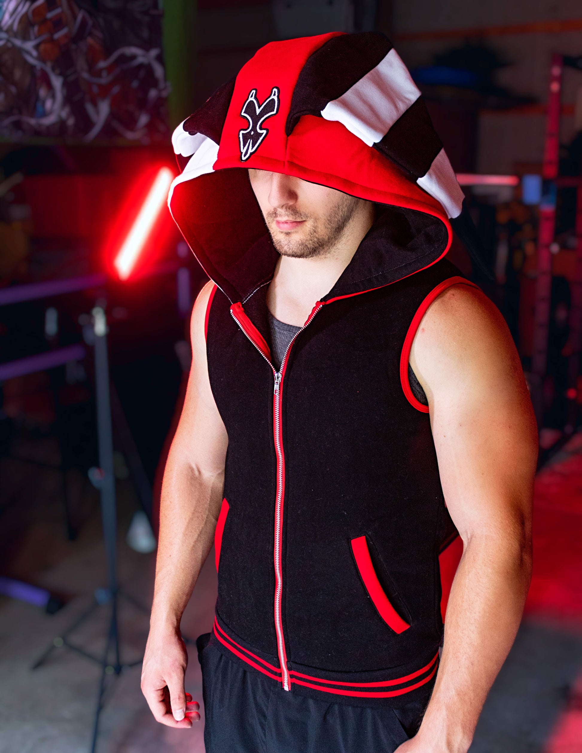 Person wearing a black, red, and white hoodie with a logo on a blurred background. Blitz cosplay inspired by Helluva Boss. sleevelss hoodie