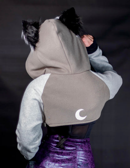 Person wearing a gray hoodie with a moon emblem on a dark background. Shrug is inspired by Loona from Helluva Boss