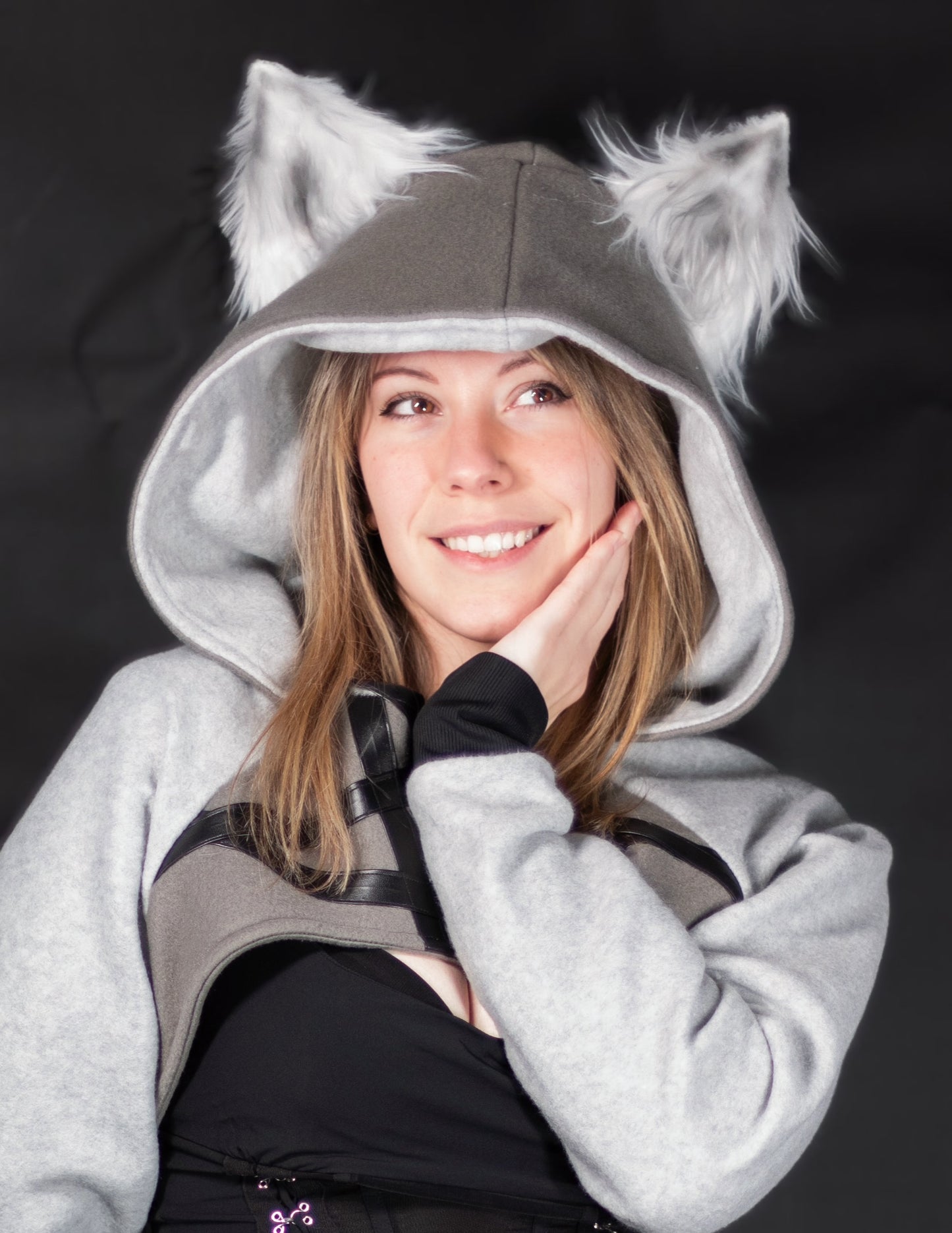 Person wearing a gray hoodie with wolf ears against a black background. Shrug is inspired by Loona from Helluve Boss.