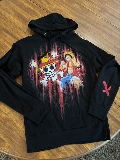 Black hoodie with a colorful graphic design on a wooden surface. Inspired by Luffy from One Piece. 