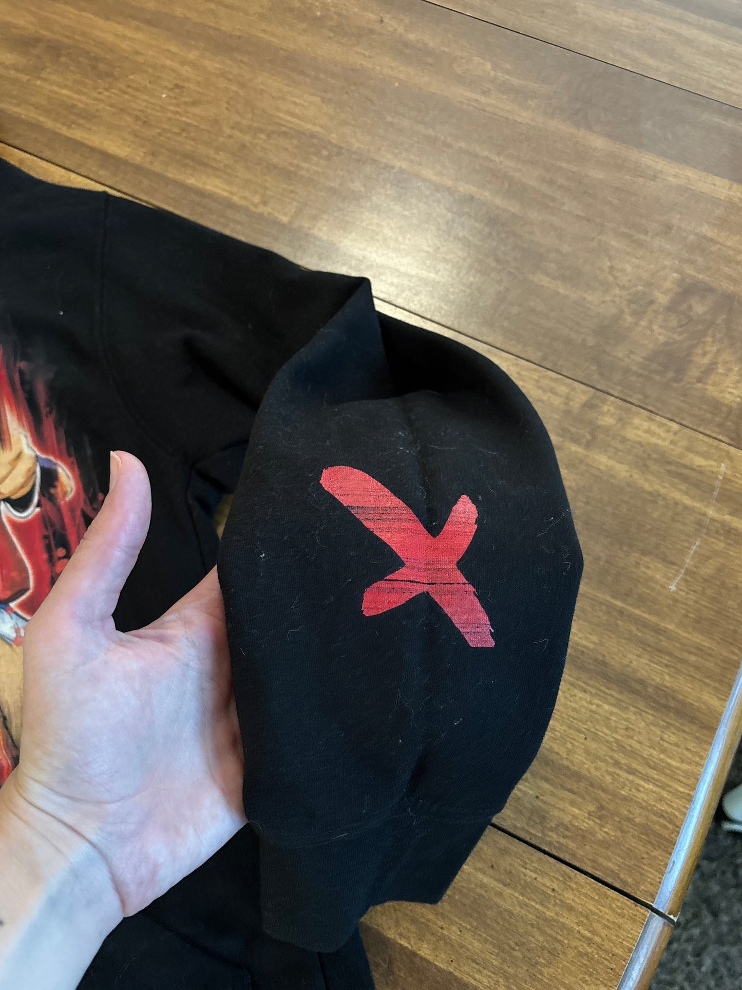close up of a Black hoodie with a colorful graphic design on a wooden surface. Inspired by Luffy from One Piece. 