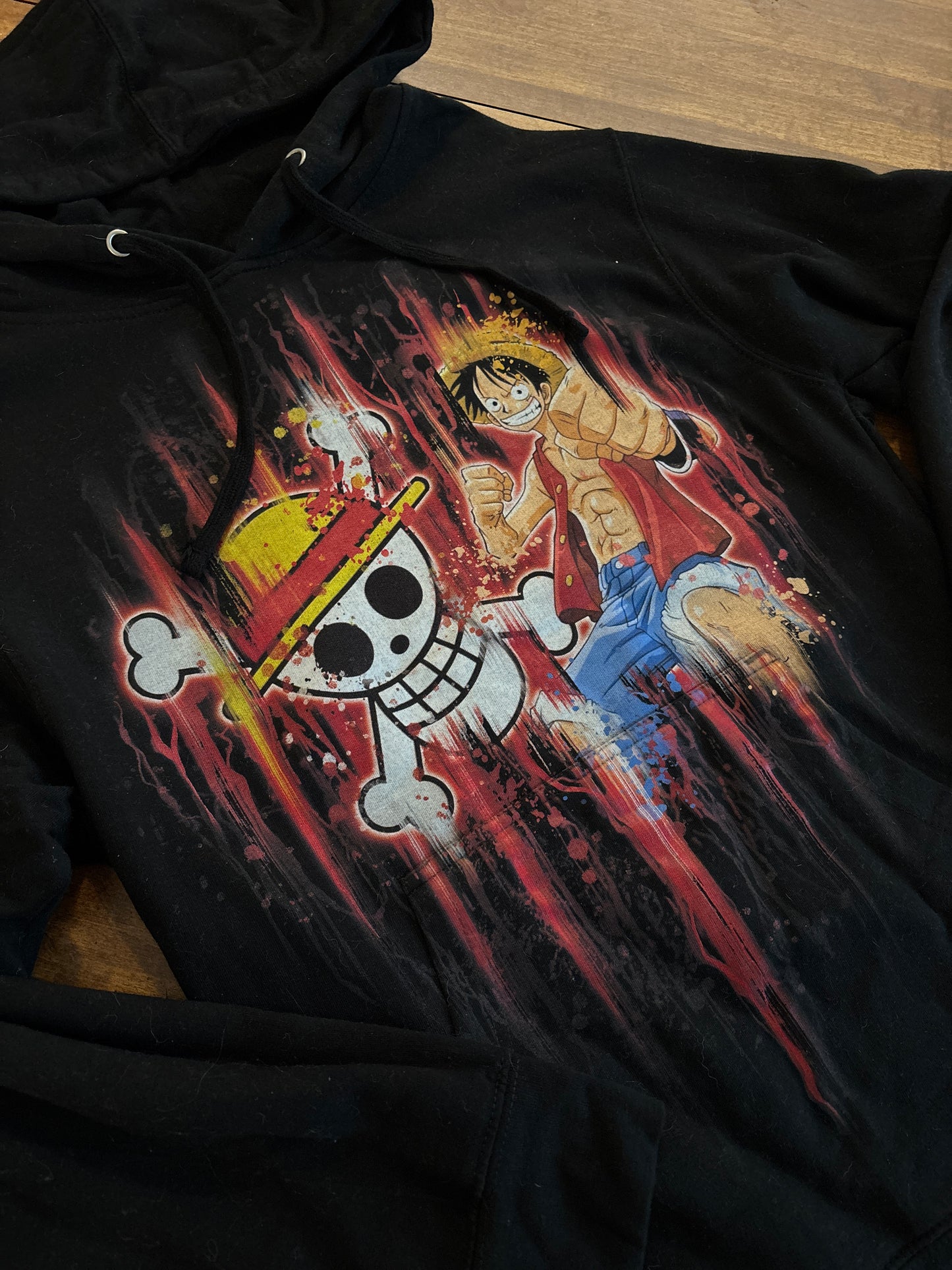 Black hoodie with a colorful graphic design on a wooden surface. Inspired by Luffy from One Piece. 