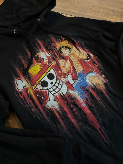 Black hoodie with a colorful graphic design on a wooden surface. Inspired by Luffy from One Piece. 