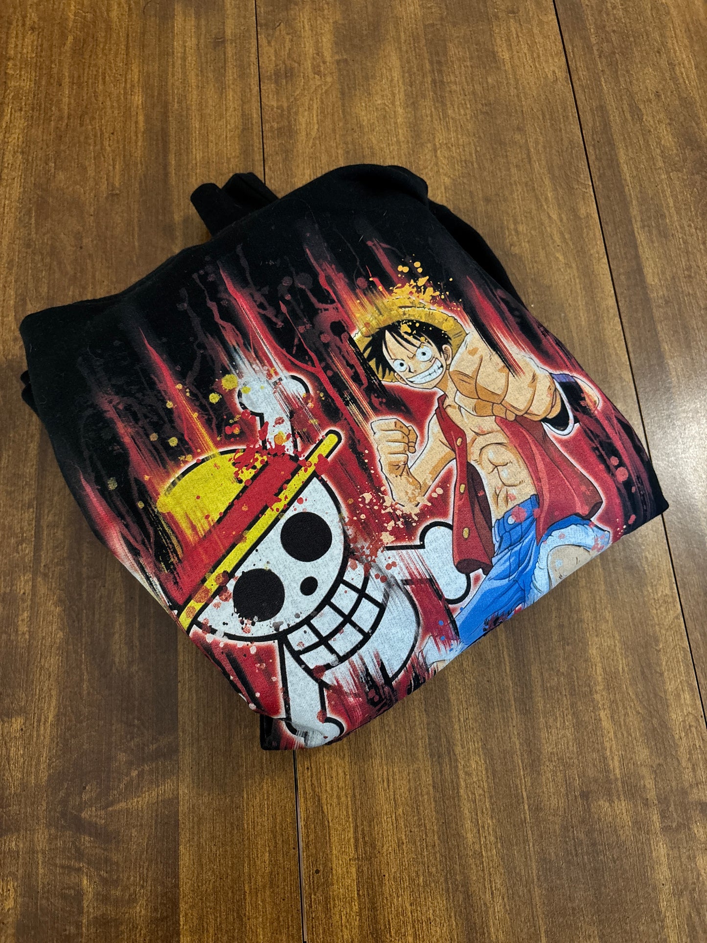 Black hoodie with a colorful graphic design on a wooden surface. Inspired by Luffy from One Piece. 
