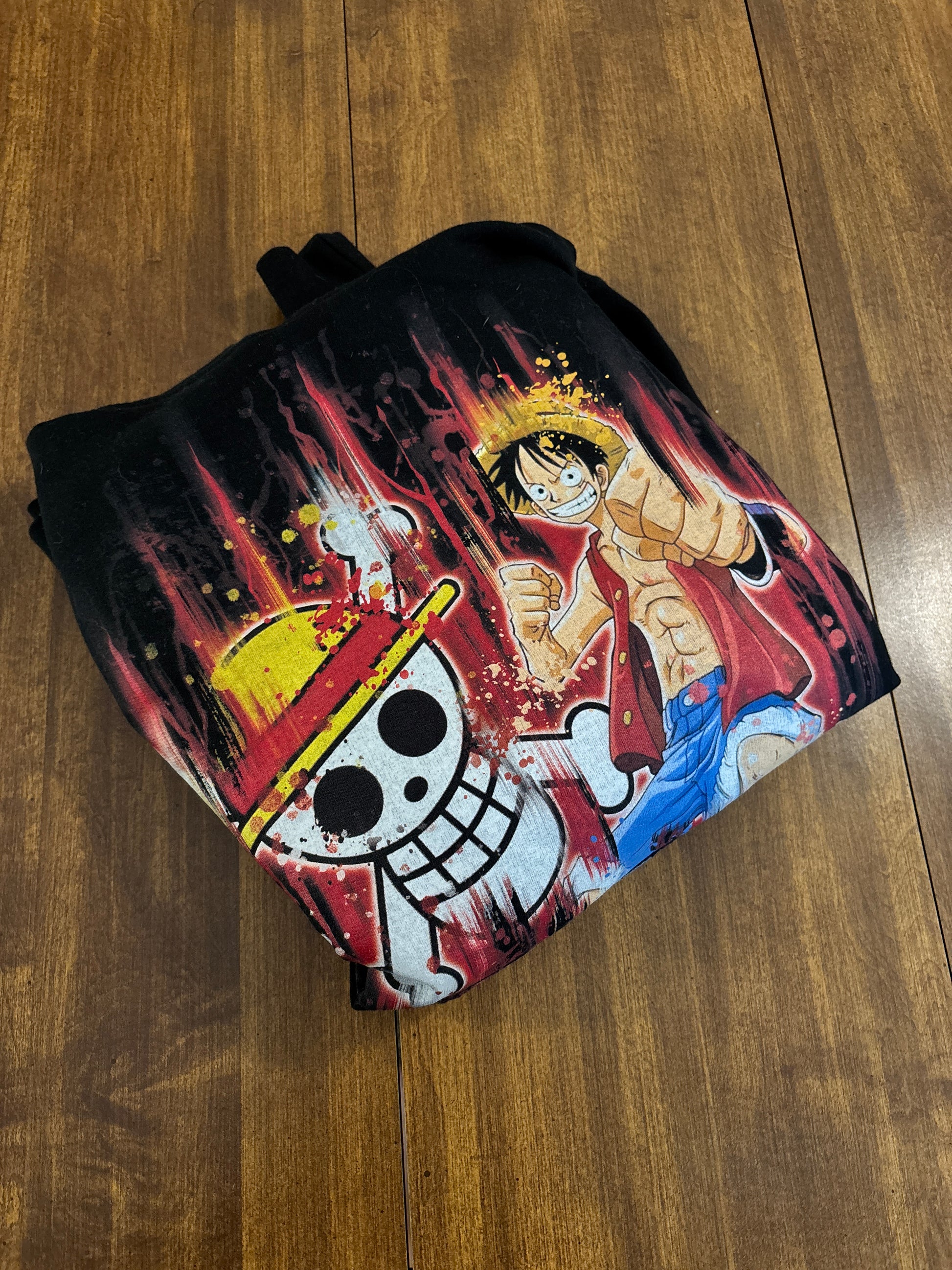 Black hoodie with a colorful graphic design on a wooden surface. Inspired by Luffy from One Piece. 