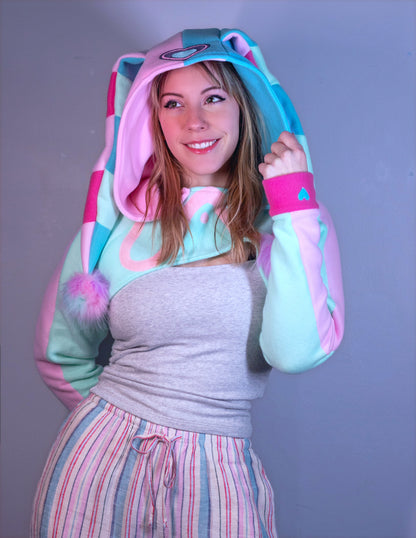 woman wearing a cropped hoodie cosplay shrug inspired by Fizzarolli from Helluva Boss in pastel colors. 