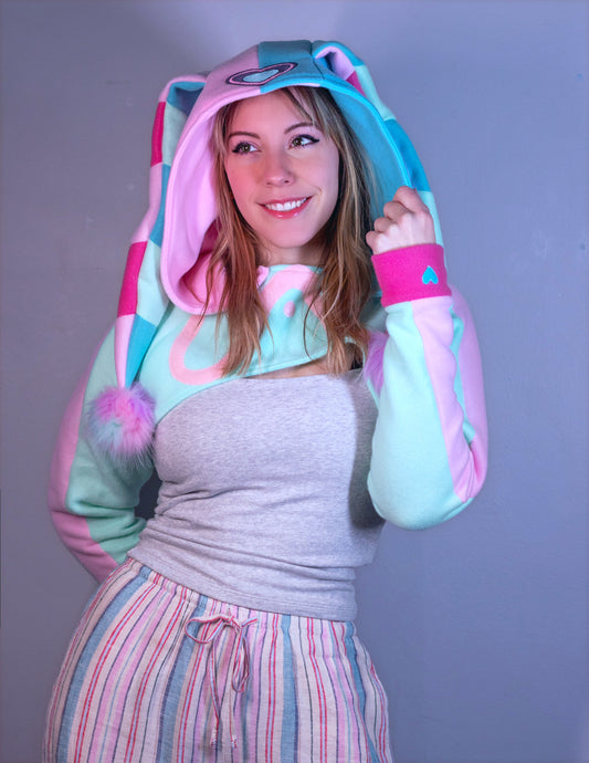 woman wearing a cropped hoodie cosplay shrug inspired by Fizzarolli from Helluva Boss in pastel colors. 