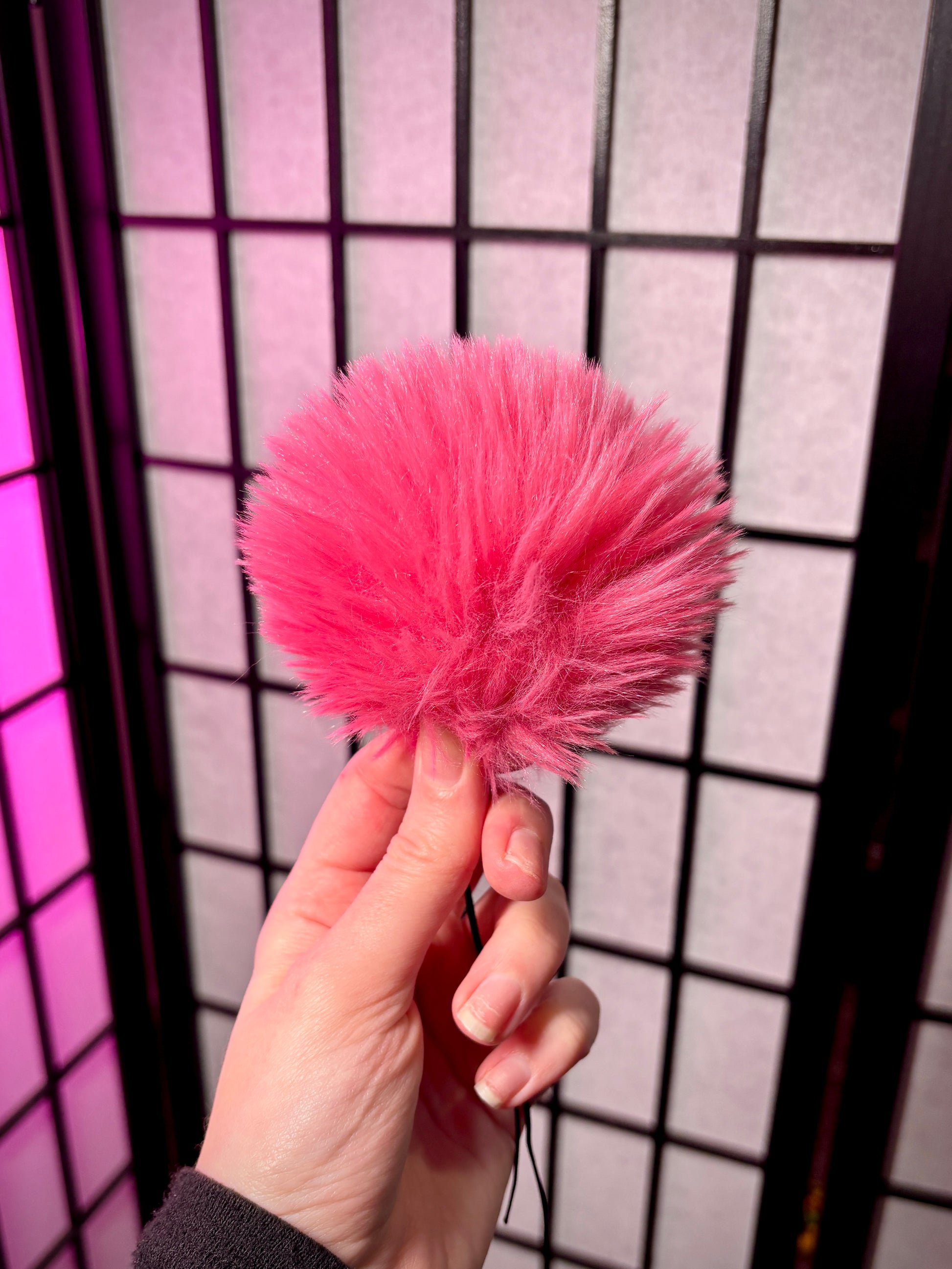 pink fur pom photographed against a grid background. Fur is all one color pink. 