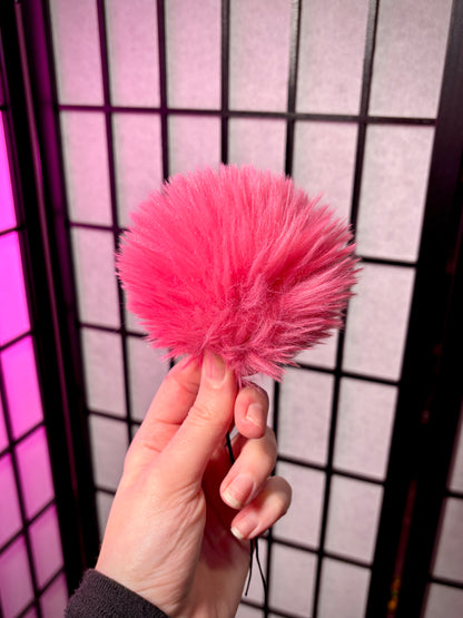 pink fur pom photographed against a grid background. Fur is all one color pink. 