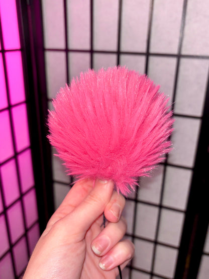 pink faux fur pom photographed with flash against a grid background. Fur is all one tone of hot pink. 