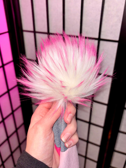 white faux fur poom with pink tips photographed against a pink and white grid background. Same pom from our VDay Fizzarolli