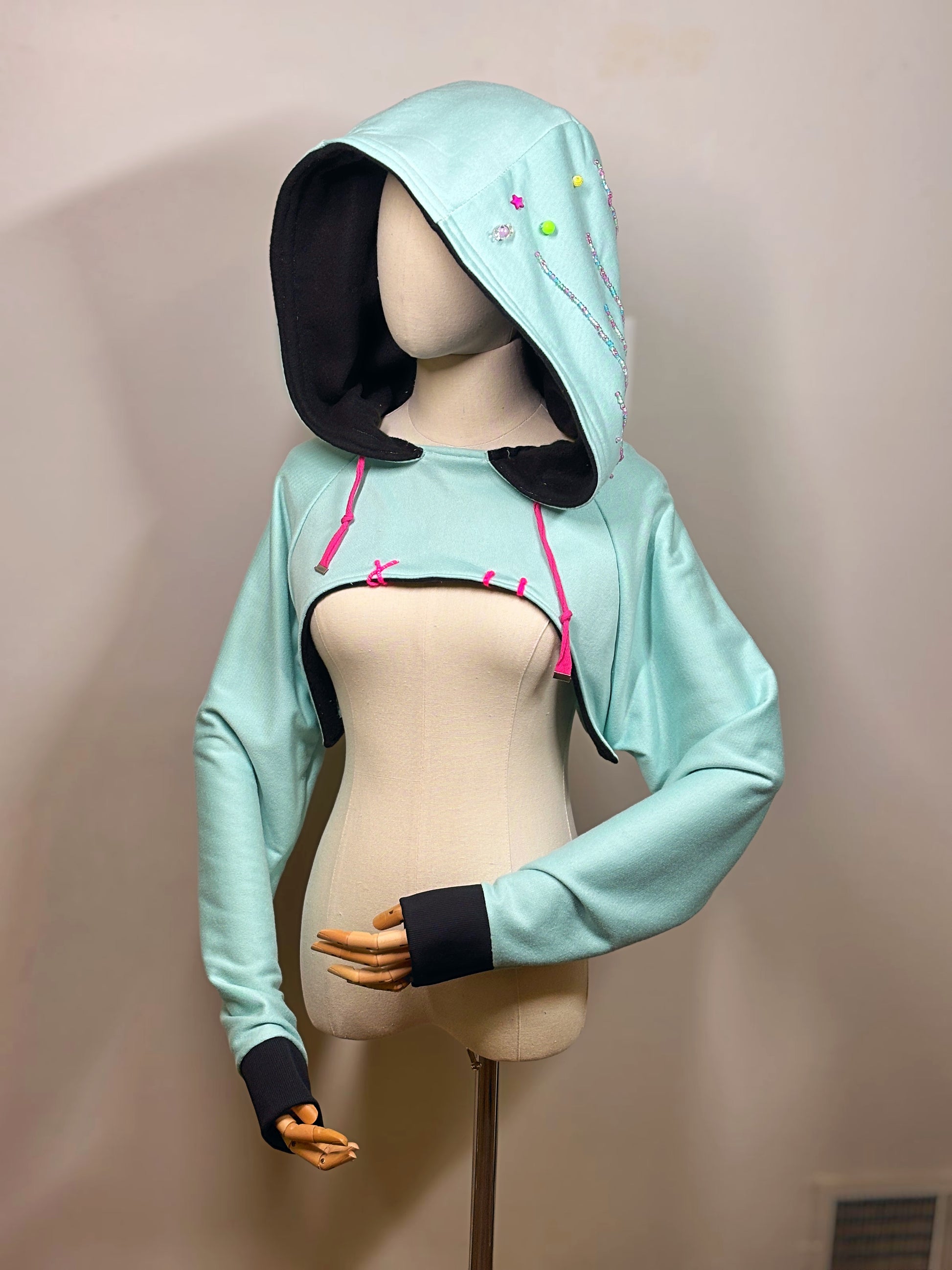 Light blue hoodie with black cuffs and pink drawstrings on a mannequin against a beige background. Inspired by  Vanellope von Schweetz from Disney's Wreck it Ralph. Perfect Cosplay Shrug.