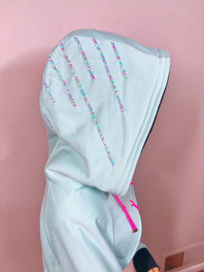 Light blue hoodie with black cuffs and pink drawstrings on a mannequin against a beige background. Inspired by  Vanellope von Schweetz from Disney's Wreck it Ralph. Perfect Cosplay Shrug.
